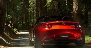 Red Mazda Miata driving on a road in a wooded area | Houston, TX